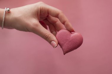 Hand holding pink macaroon in the heart shape
