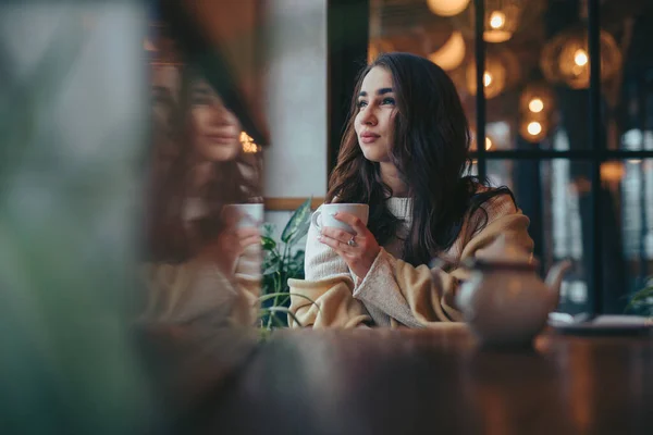 Nuori nainen juo teetä kahvilassa katselee ikkunasta — kuvapankkivalokuva