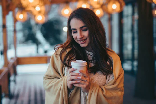ผู้หญิงสวยถือถ้วยกาแฟกระดาษบนระเบียงคาเฟ่ในวันฤดูหนาว — ภาพถ่ายสต็อก