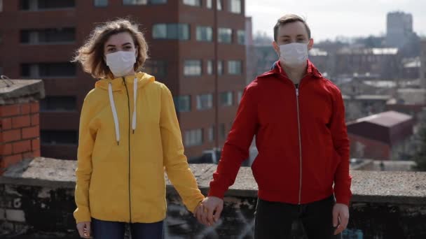 Virus epidemic, woman and man in surgical masks holding hands on the roof of city — Stockvideo