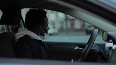 Cerrahi maskeli Afrikalı Amerikalı bir adam arabanın camını açıyor.