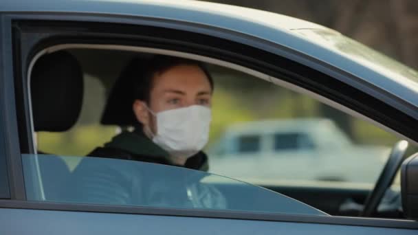 Hombre con máscara quirúrgica mirando por la ventana de un coche — Vídeo de stock