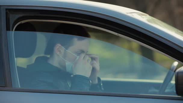 Людина в хірургічній масці дивиться через вікно в машині — стокове відео