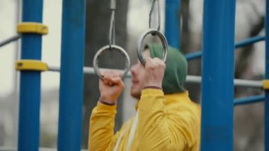 Parktaki halkalarda barfiks çeken adam.