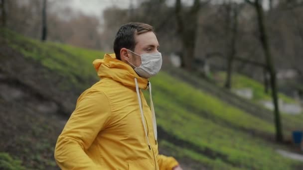 Человек в парке носит капюшон в хирургической маске — стоковое видео