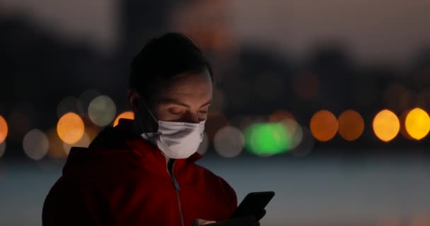 Virusepidemi, man använder smartphone med kirurgisk mask på kvällen staden — Stockvideo