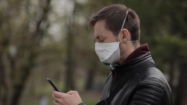 Человек, использующий смартфон с хирургической маской в парке — стоковое видео
