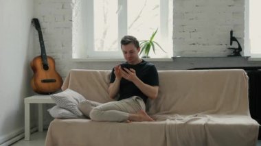 Akıllı telefon arayan adam evdeki kanepede oturuyor.