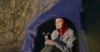 Kamp yapan kadın çadırda oturmuş termostan çay içiyor.