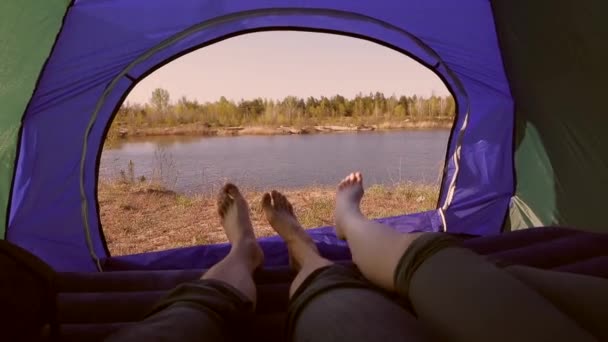 Casal deitado em uma tenda de acampamento, pernas masculinas e femininas com vista para o lago — Vídeo de Stock