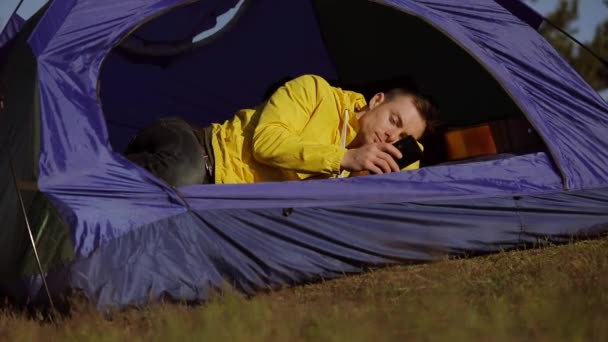 Homem relaxante em uma tenda de acampamento com smartphone — Vídeo de Stock