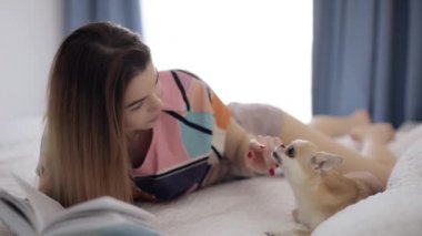 Evde kitap okuyan bir kadın köpekle oynuyor.