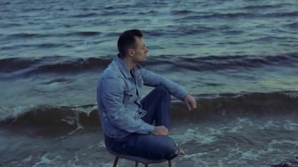 Samotny człowiek siedzący na krześle w burzliwych falach morskich — Wideo stockowe