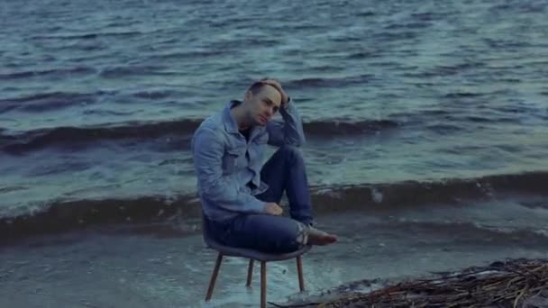 Fırtınalı deniz dalgalarında sandalyede oturan yalnız bir adam. — Stok video