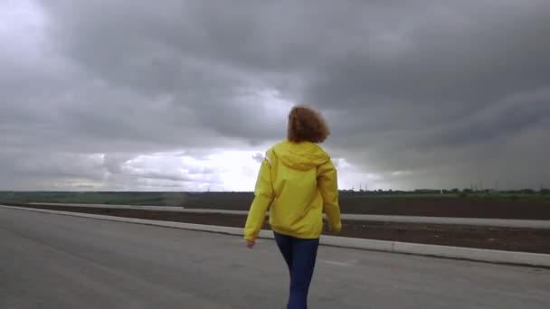 Женщина в жёлтой куртке смотрит на облака в пасмурный день — стоковое видео
