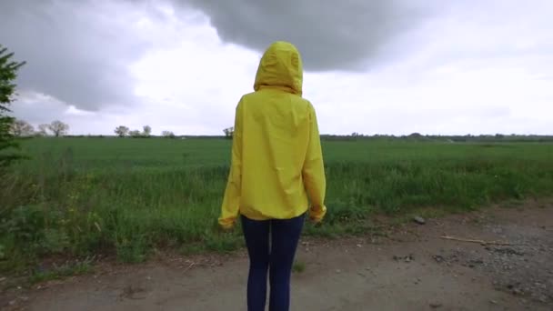 Женщина в жёлтой куртке смотрит на облака в пасмурный день — стоковое видео