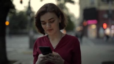 Şehir caddesinde yürürken akıllı telefonla mesajlaşan bir kadın.