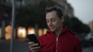 Şehir caddesinde yürürken akıllı telefonla mesajlaşan adam.