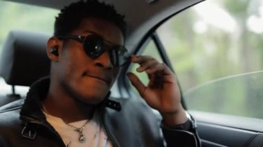Havalı Afrikalı Amerikalı adam arabada oturmuş müzik dinliyor.