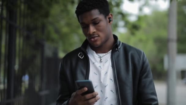 Afroamerikansk man tittar på smartphone promenader i sommar stad — Stockvideo