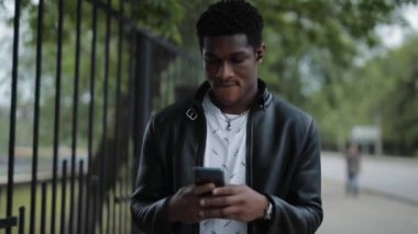 Afrika kökenli Amerikalı bir adam yaz şehrinde yürürken akıllı telefona bakar.