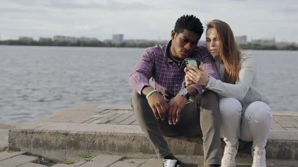 Två multiraciala vänner tittar ner i smartphone — Stockvideo