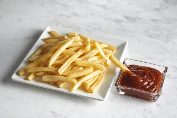 French fries in a diagonal square dish with potato in a ketchup pot