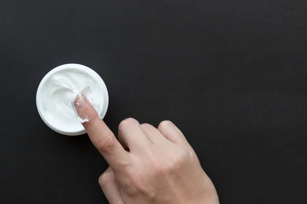 Crema para cara o cuerpo en recipiente blanco y mano femenina en bla — Foto de Stock