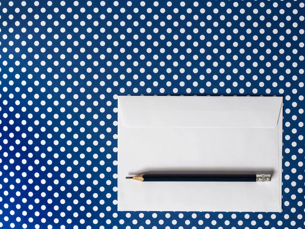 Envelope de papel branco e lápis preto em uma polca de fundo azul — Fotografia de Stock