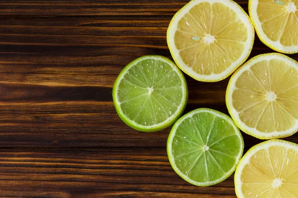 Slices of fresh lemons and limes on brown wooden table. Pattern — Stock Photo, Image