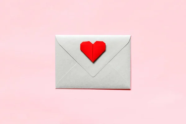 Silver envelope and origami heart on pink background.