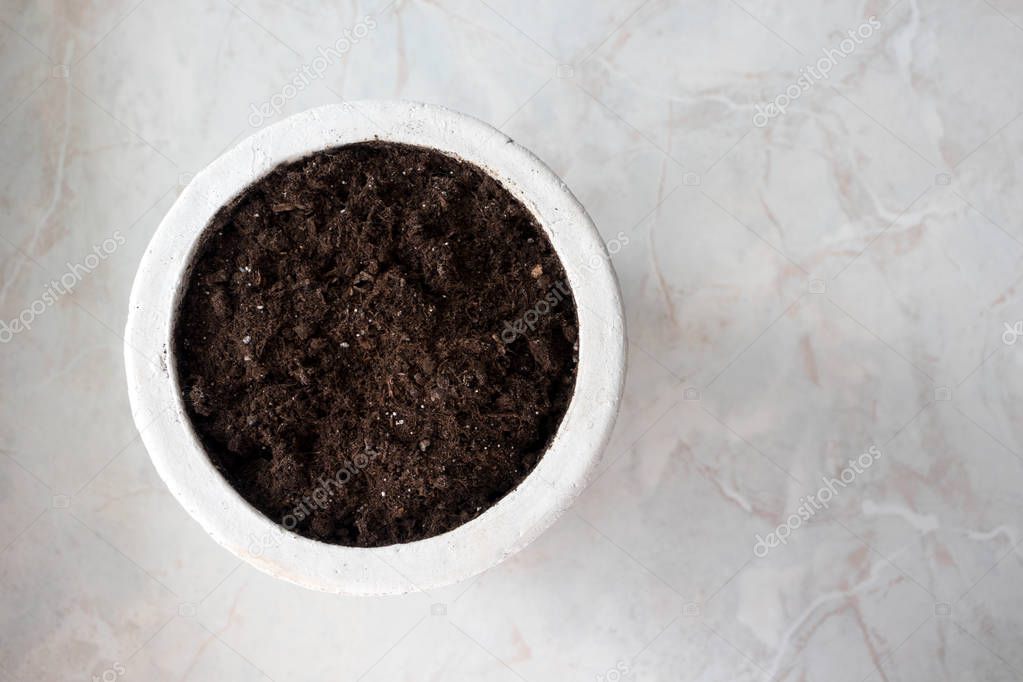 Flower pot with soil on marble background, top view. Indoor gard