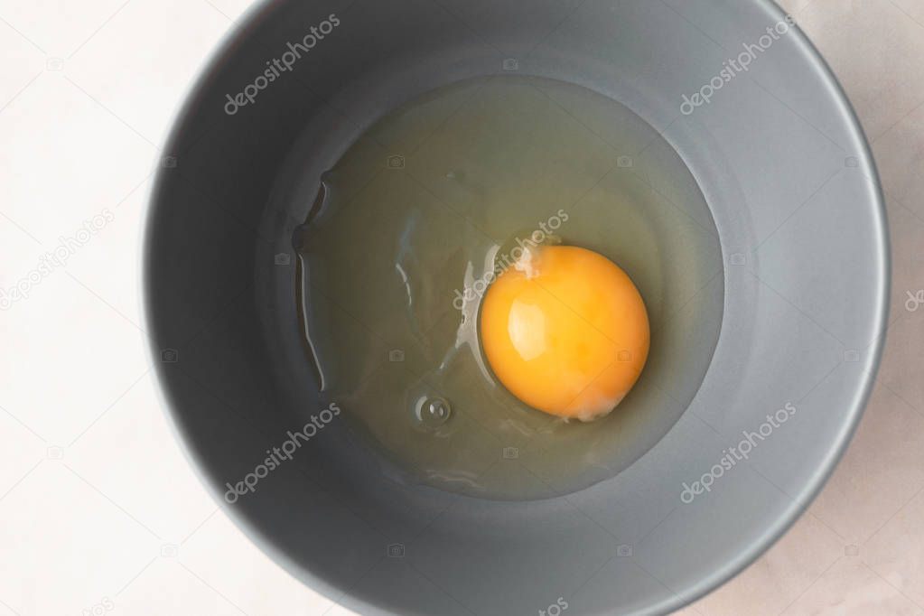 Raw uncooked egg in gray bowl, top view. Yellow egg yolk and liquid egg whites. Ingredient for baking, scrambled eggs or omelet