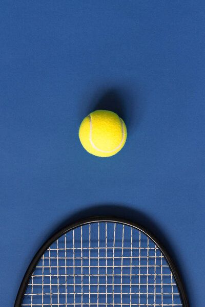 Yellow tennis ball and black racket on blue background. Color of