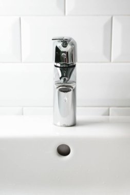 Musluktan damlayan su beyaz seramik lavaboya ve beyaz fayans duvarına, dikey. Modern banyo, yaşam tarzı.