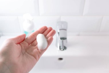 Elinde sabun köpüğü var. Banyodaki lavabonun üstünde ellerini yıkıyorsun., 