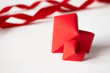 Beyaz arka planda iki kırmızı origami kalbi ve saten kurdele 