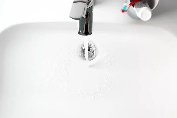 Water flows from the tap into white ceramic sink and glass with — Stock Photo, Image