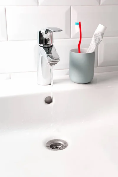 Flowing water in white sink and toothbrush in domestic bathroom, — Stock Photo, Image