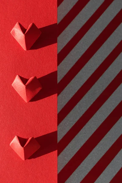 Corações de origami vermelho no fundo de papel e listras de brilho prata — Fotografia de Stock