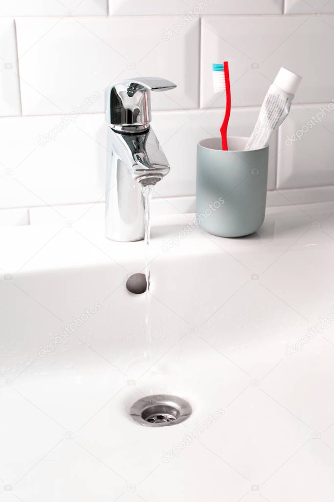 Flowing water in white sink and toothbrush in domestic bathroom,