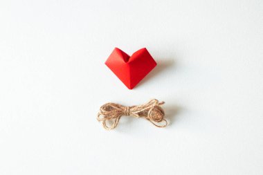 Bir kırmızı origami kalp şekli ve ip ip beyaz torbaya izole edilmiş.