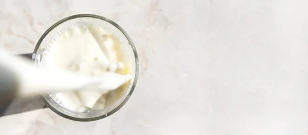 Freshness milk filling glass on marble table background with copy space, above. Drink splash, close-up. Dairy product banner format