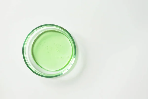 Beyaz arka planda cam petri kabında şeffaf yeşil şampuan ya da yüz temizleyici. Laboratuvar testlerini ve araştırmalarını kabul et, doğal kozmetik ürünleri yap.