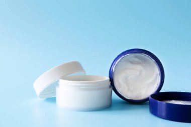 Mavi arka planda beyaz plastik kavanozlarda açık nemlendirici krem. Model kozmetik markalaşma