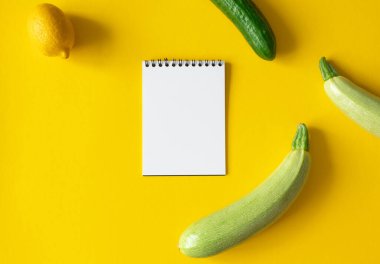 Boş beyaz not defteri, kabak, limon ve salatalık sarı arka planda ve mesaj için yer var. Model bildiri tarifi ya da yemek planı, üst görünüm