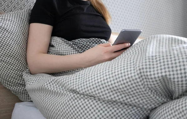 Close-up caucasian ethnicity woman holding smartphone with selective focus at bed. Lifestile