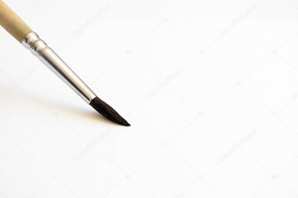 Close-up paintbrush on white watercolor paper with selective focus and copy space, horizontal. Hobby and art tool