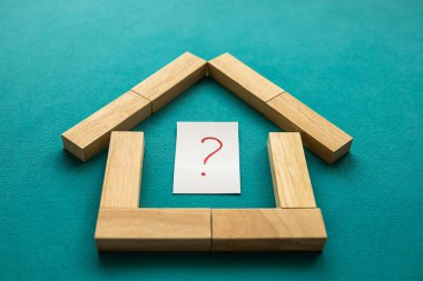 Ahşap bloklardan yapılmış bir ev. Mavi arka planda kırmızı soru işareti var. Düşük açı görünümü, yakın plan.