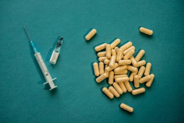 Sarı haplar, tıbbi şırınga ve mavi arka planda aşı ampulü. Sağlık ve tıbbi bakım kavramı. Düz konum, üst görünüm, kopyalama alanı.
